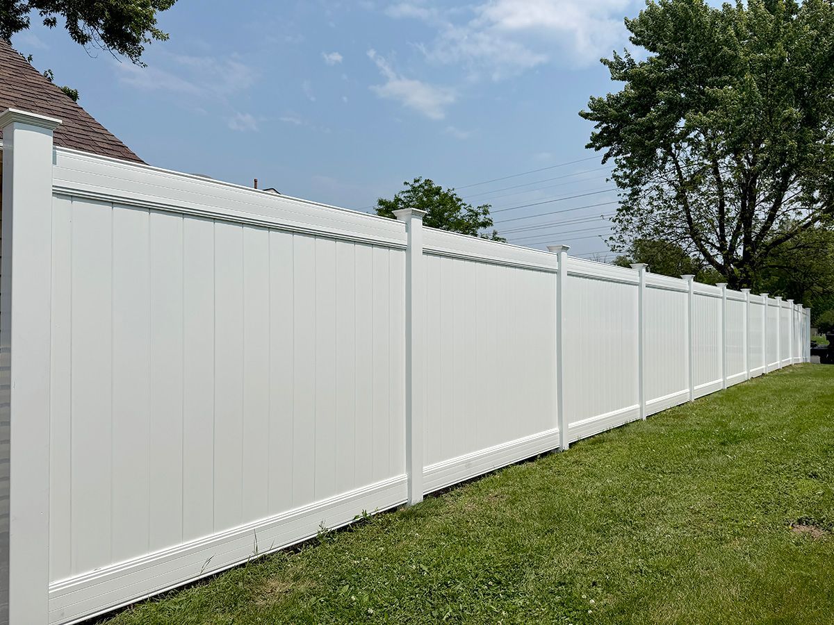 A tall, white vinyl privacy fence stands in a grassy yard under a blue sky.