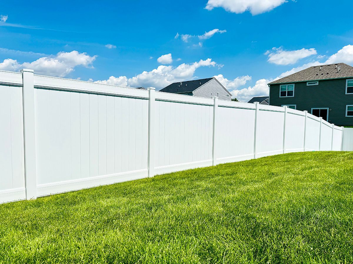 White vinyl fence along a bright green lawn under a blue sky with clouds
