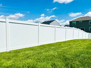 A white vinyl privacy fence lines a grassy backyard under a bright blue sky with light clouds.