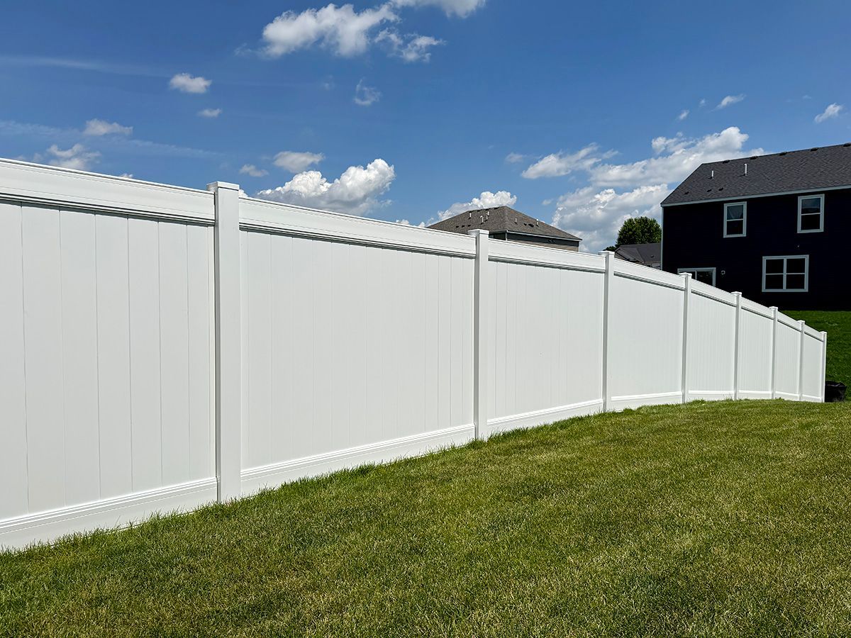 A long, white vinyl privacy fence set against a green lawn and a blue sky with clouds, next to a dark house.