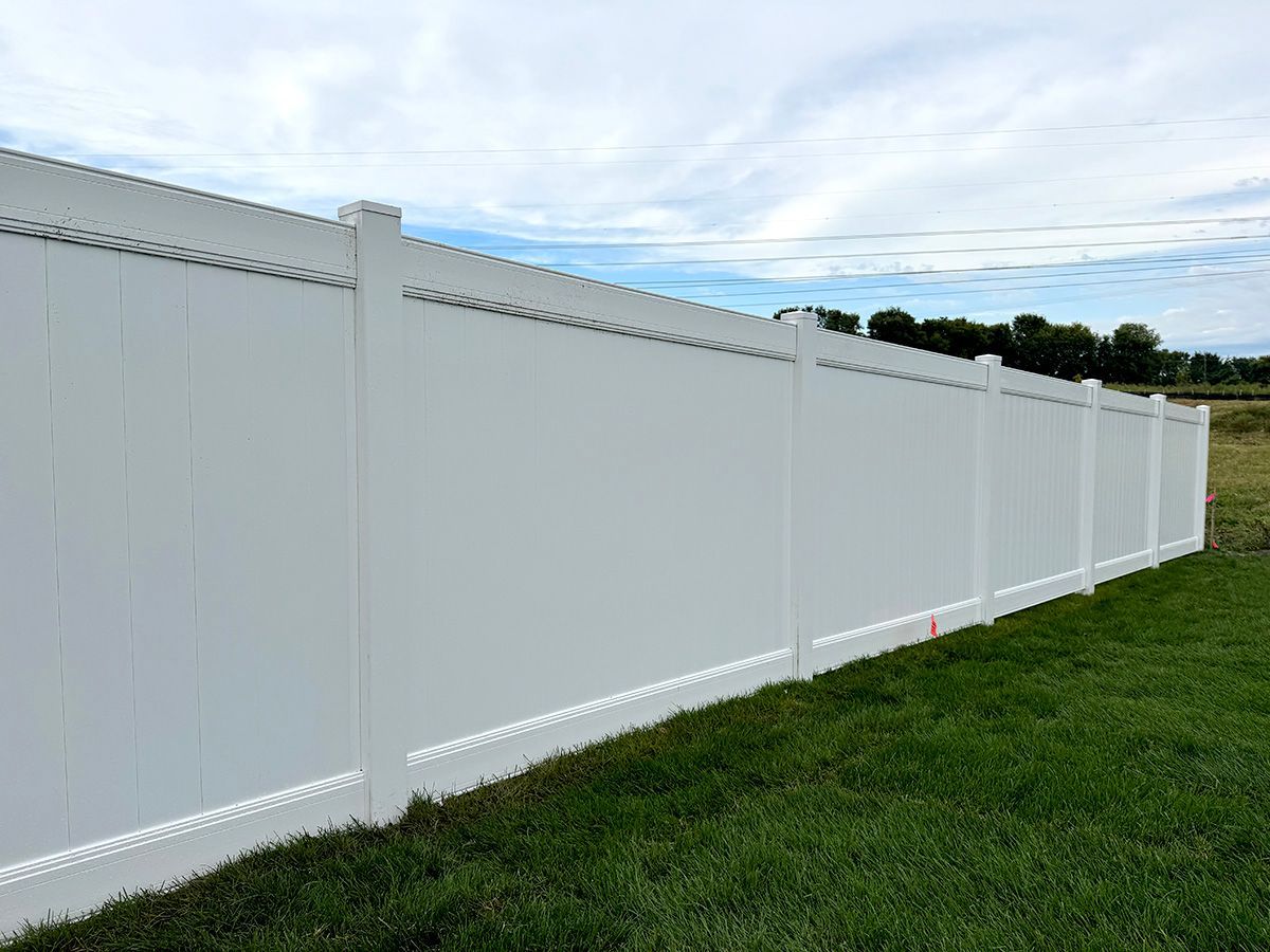 A long, white vinyl privacy fence set against a green grass lawn under a partly cloudy sky.