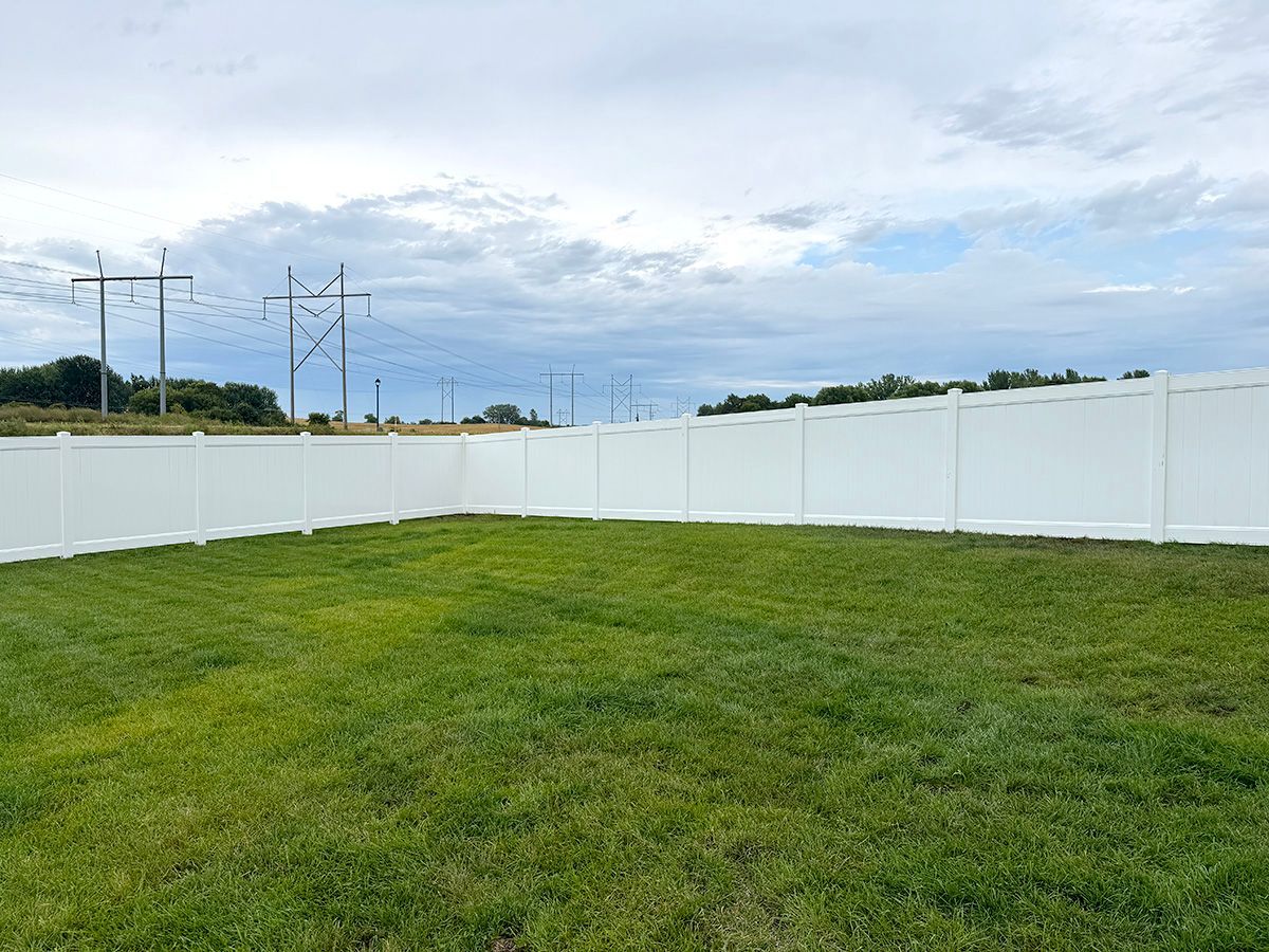 A fenced-in backyard with a green lawn under a cloudy sky.