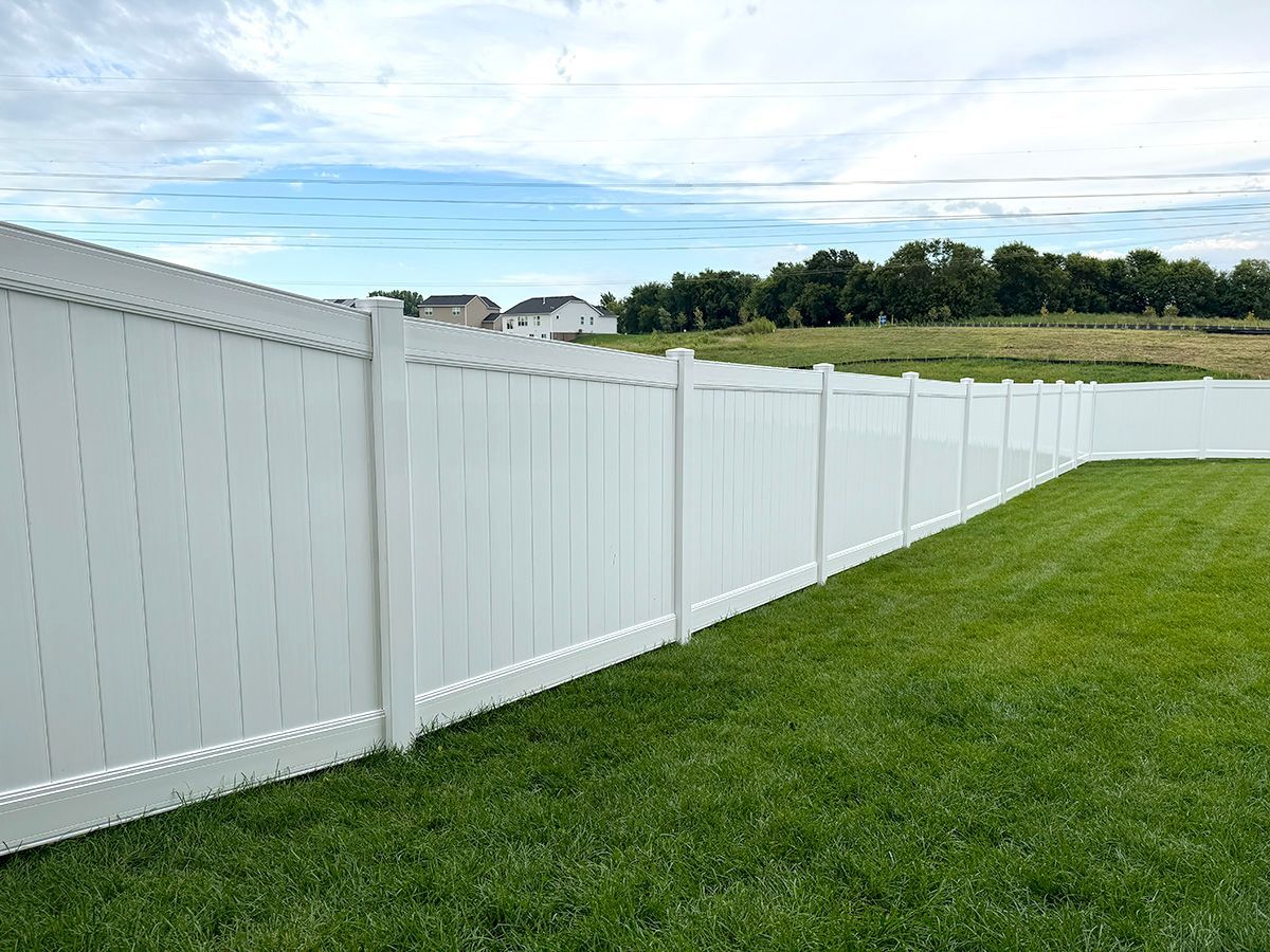 A long, white vinyl privacy fence lines the edge of a green lawn under a partly cloudy sky.