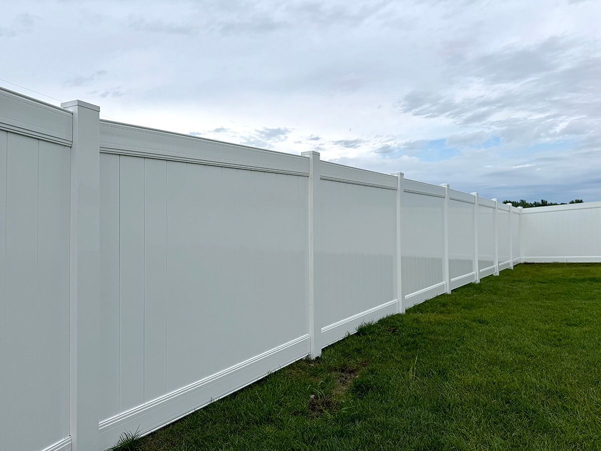 A white vinyl privacy fence lines a grassy yard against a cloudy sky.