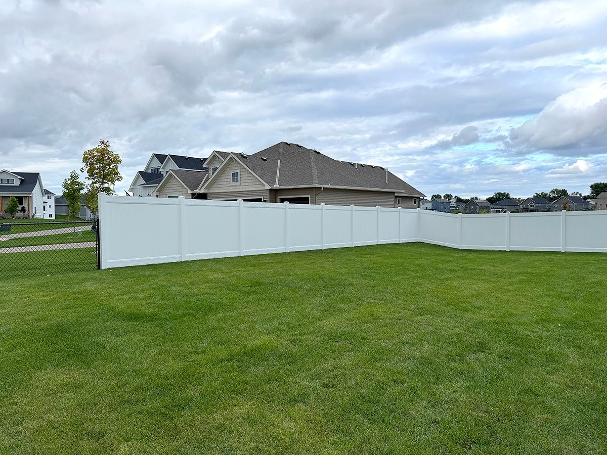 A tall white vinyl privacy fence encloses a green grassy backyard under a cloudy sky.
