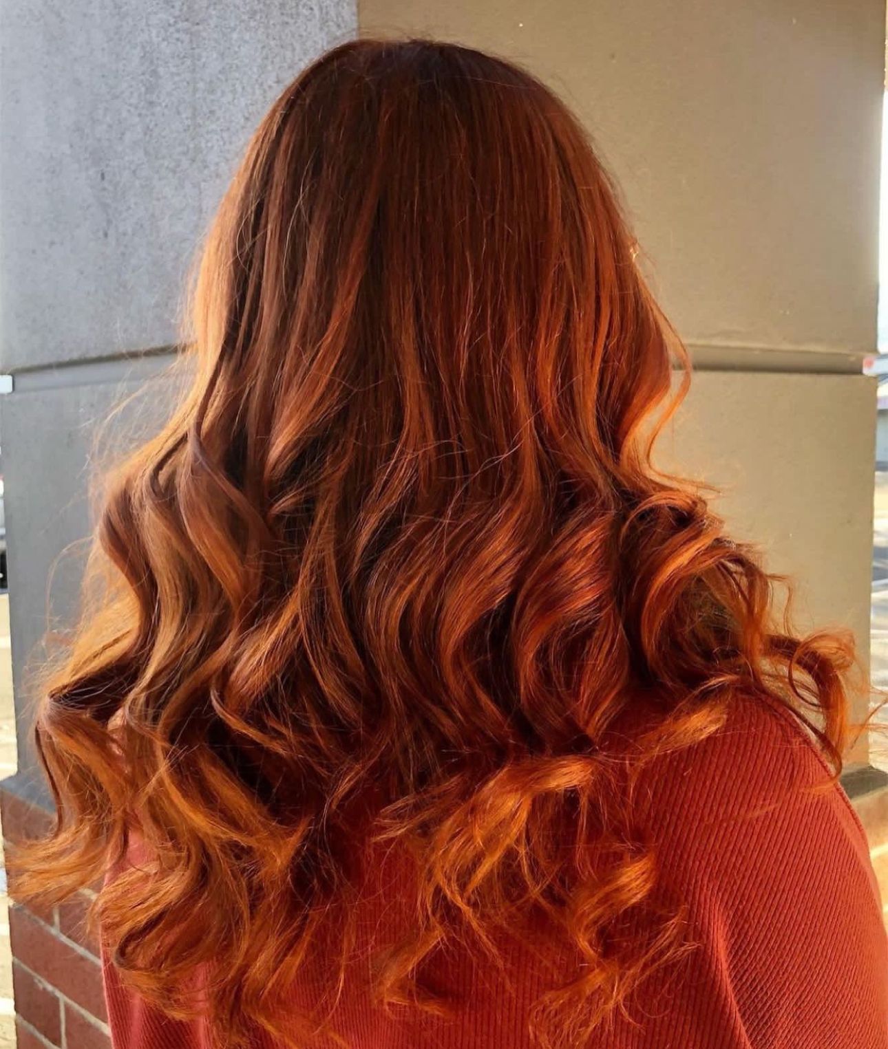 Woman with long, wavy auburn hair. Sunlight catches the highlights.