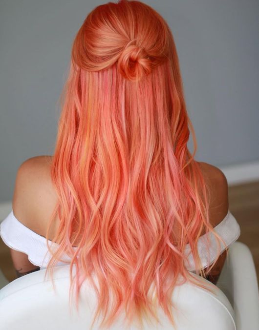 Woman with long, wavy, peach-colored hair in a half-up, looped bun style, wearing a white off-the-shoulder top.