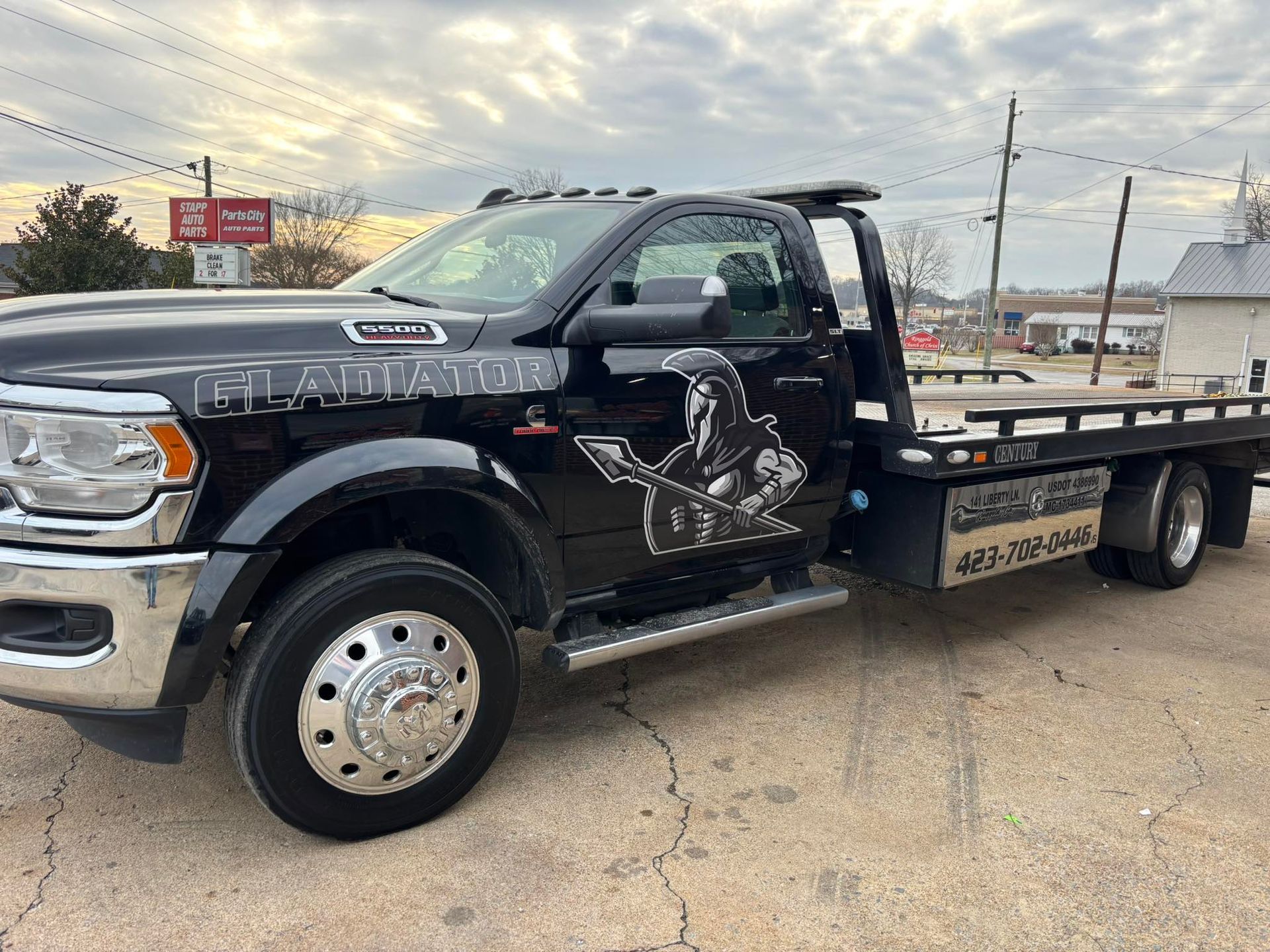 Black flatbed tow truck parked on a lot under a cloudy sky