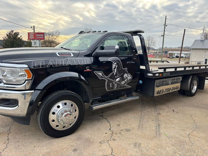 Black flatbed tow truck parked on a lot under a cloudy sky
