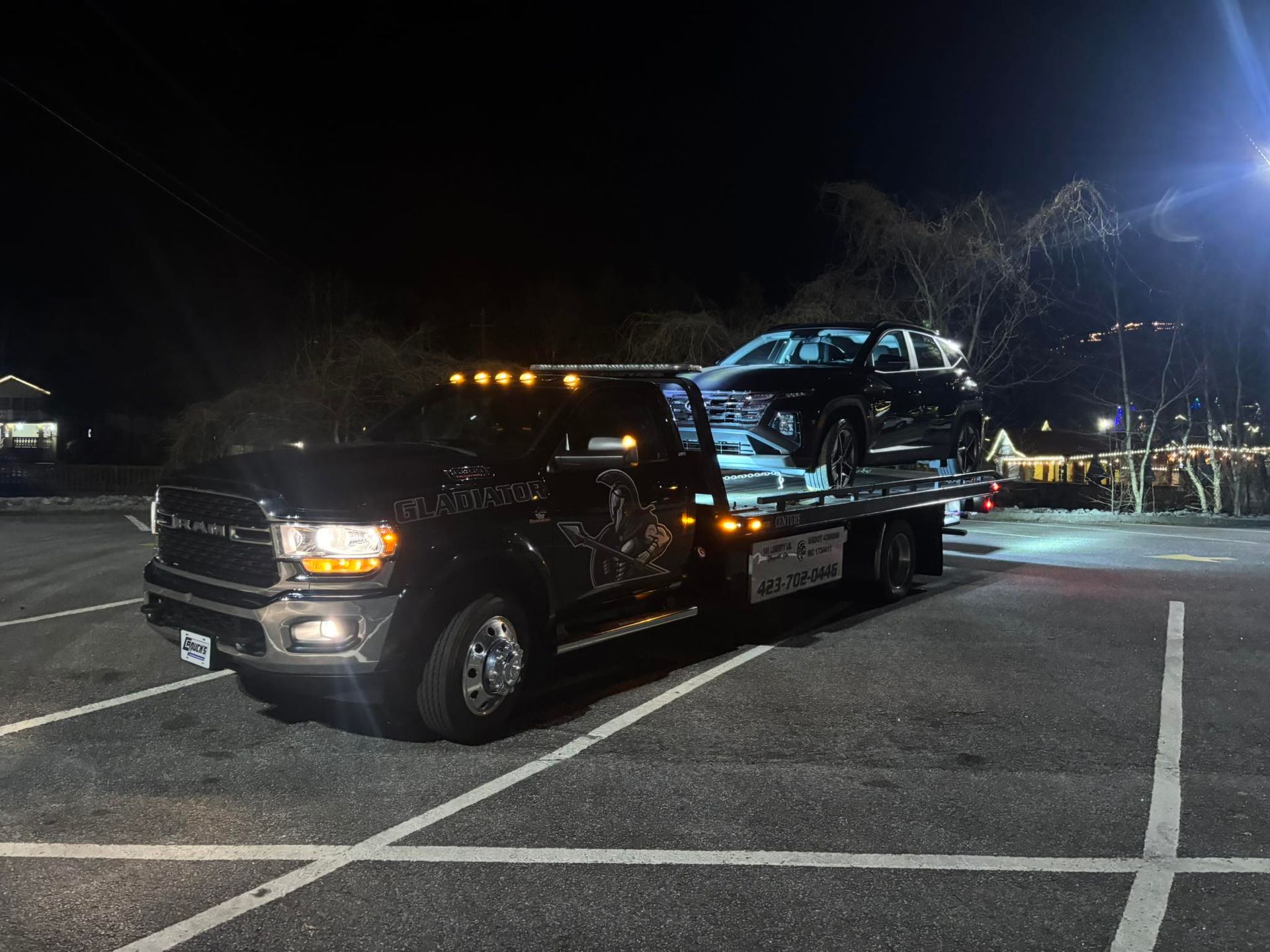 Black pickup truck towing a damaged blue car on a flatbed at night in a parking lot