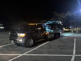 Black tow truck hauling a dark car in a parking lot at night