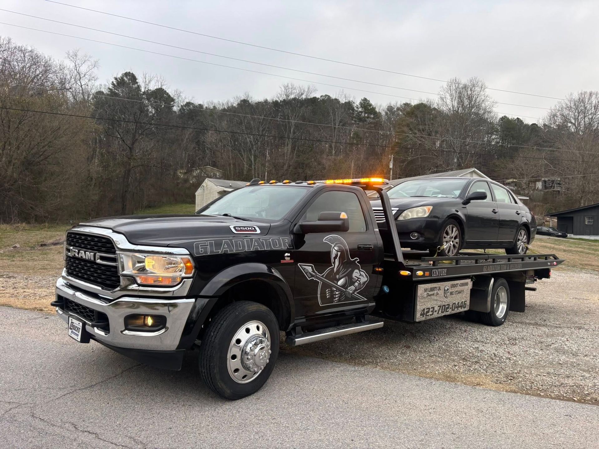 Tow truck loaded with a black pickup on a gravel road in a wooded area