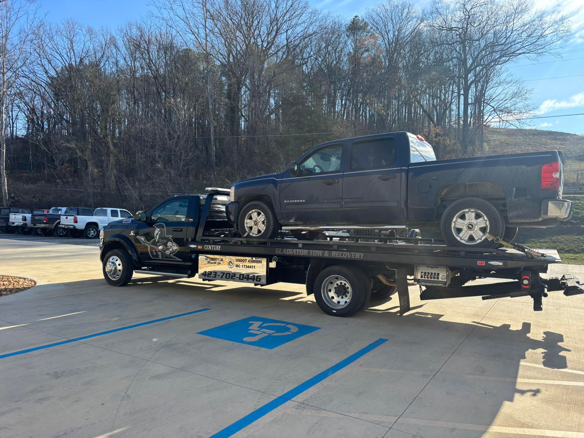 Tow truck hauling a black pickup on a flatbed in a parking lot