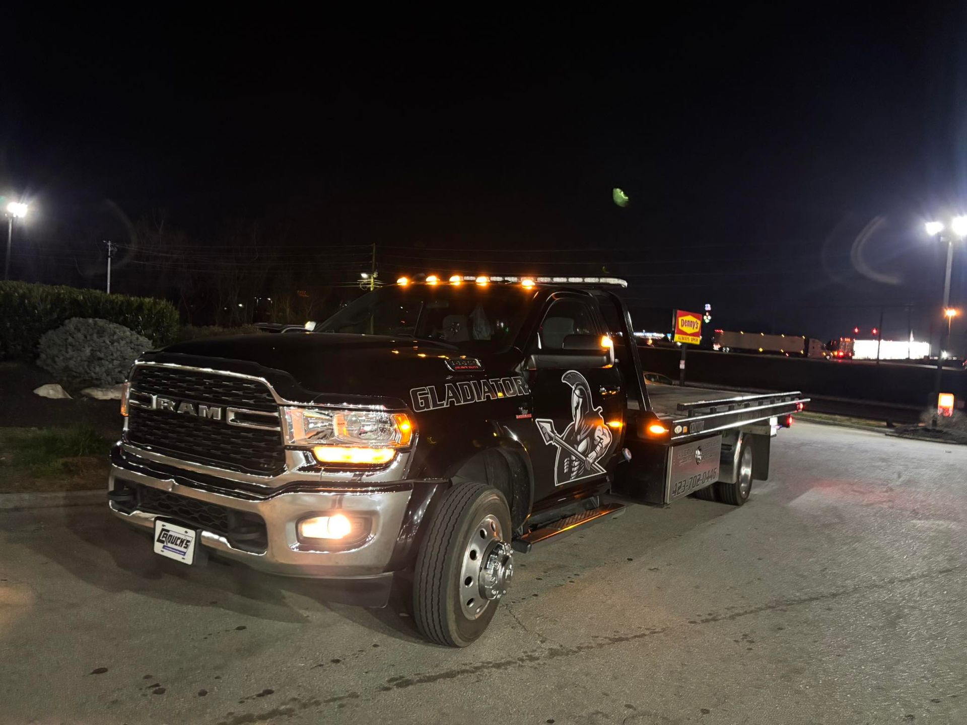 Black pickup truck parked at night in a lit lot, with headlights and amber roof lights on.