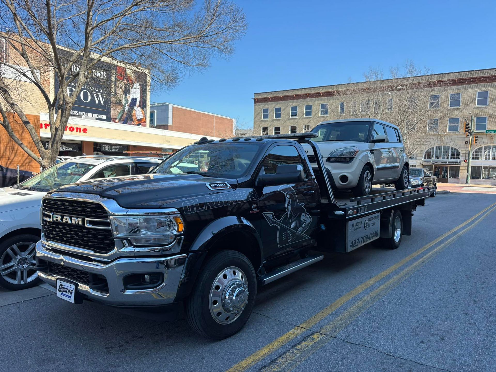 Black GMC tow truck carrying a silver SUV on a city street in daylight