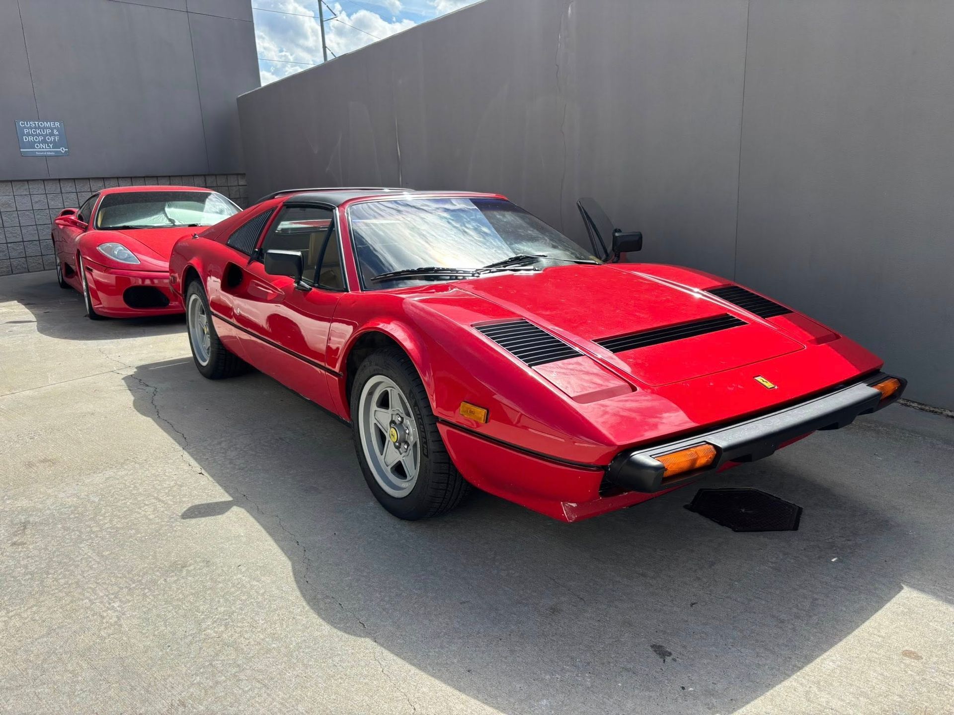 Two red sports cars parked outdoors beside a gray wall.