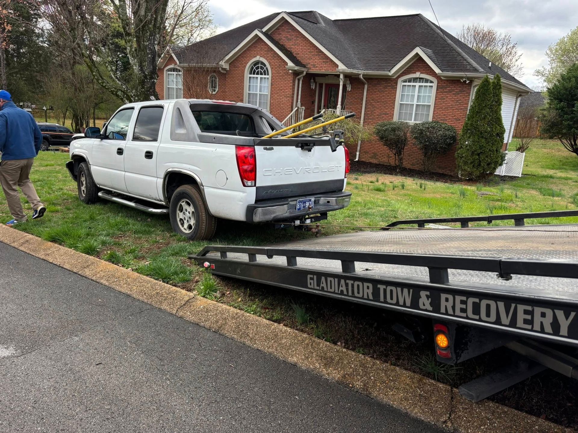 Tow truck loading a white pickup on a suburban street outside a brick house