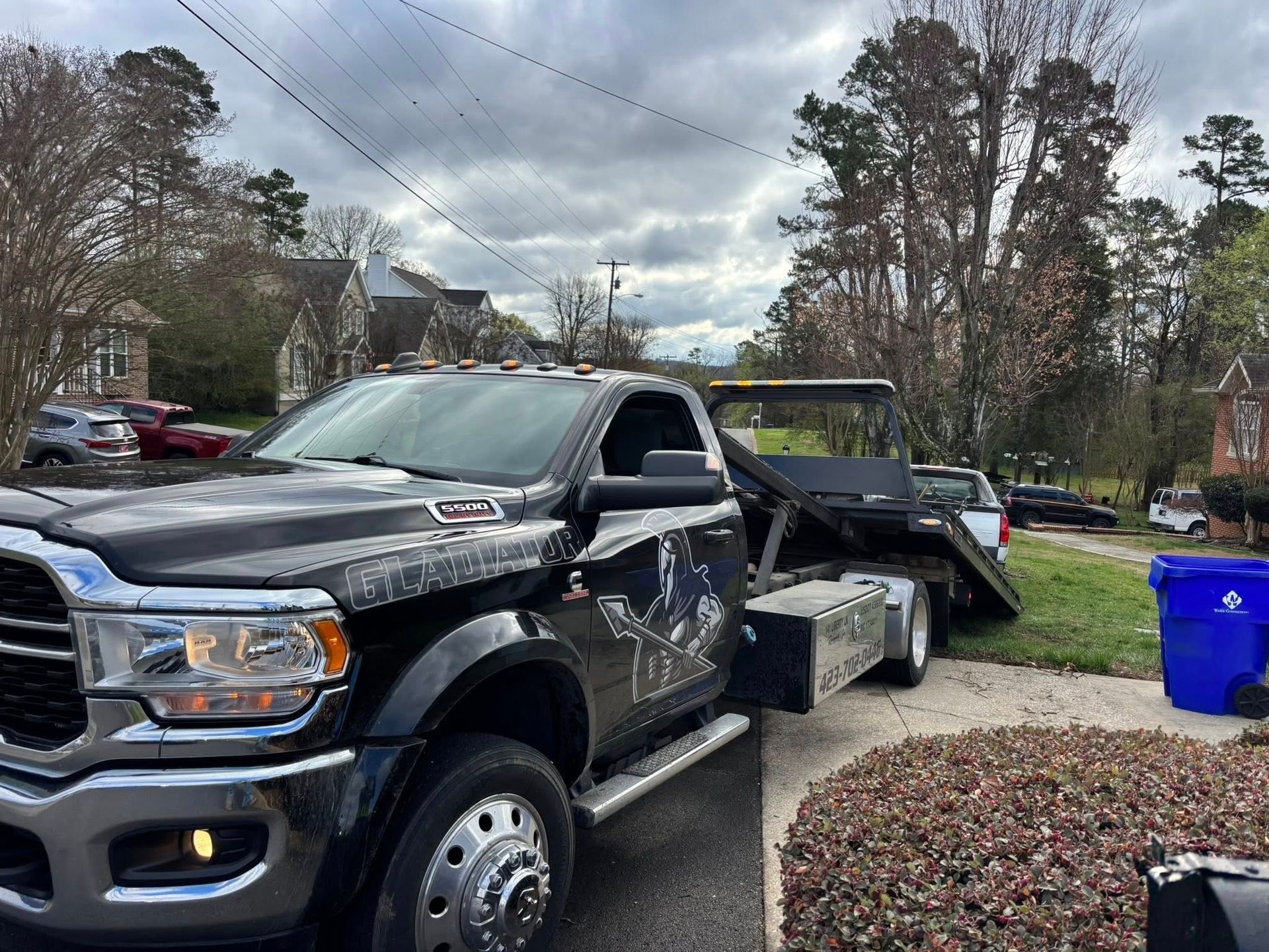 Black pickup truck loaded onto a flatbed tow truck on a roadside near houses and trees