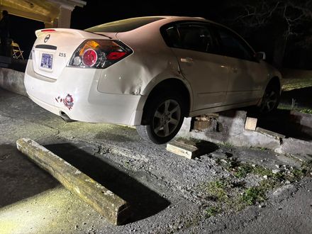 White sedan stuck on concrete blocks at night, with debris on gravel roadside.