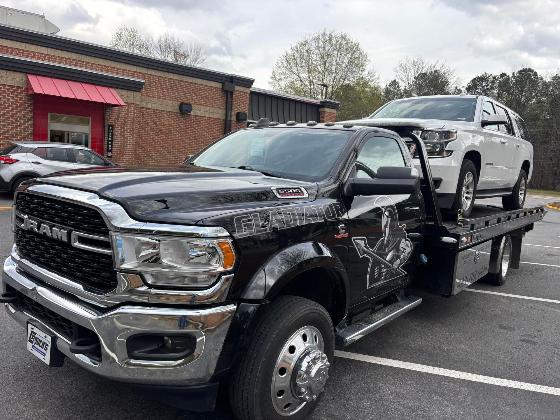 Black flatbed tow truck carrying a white SUV in a parking lot