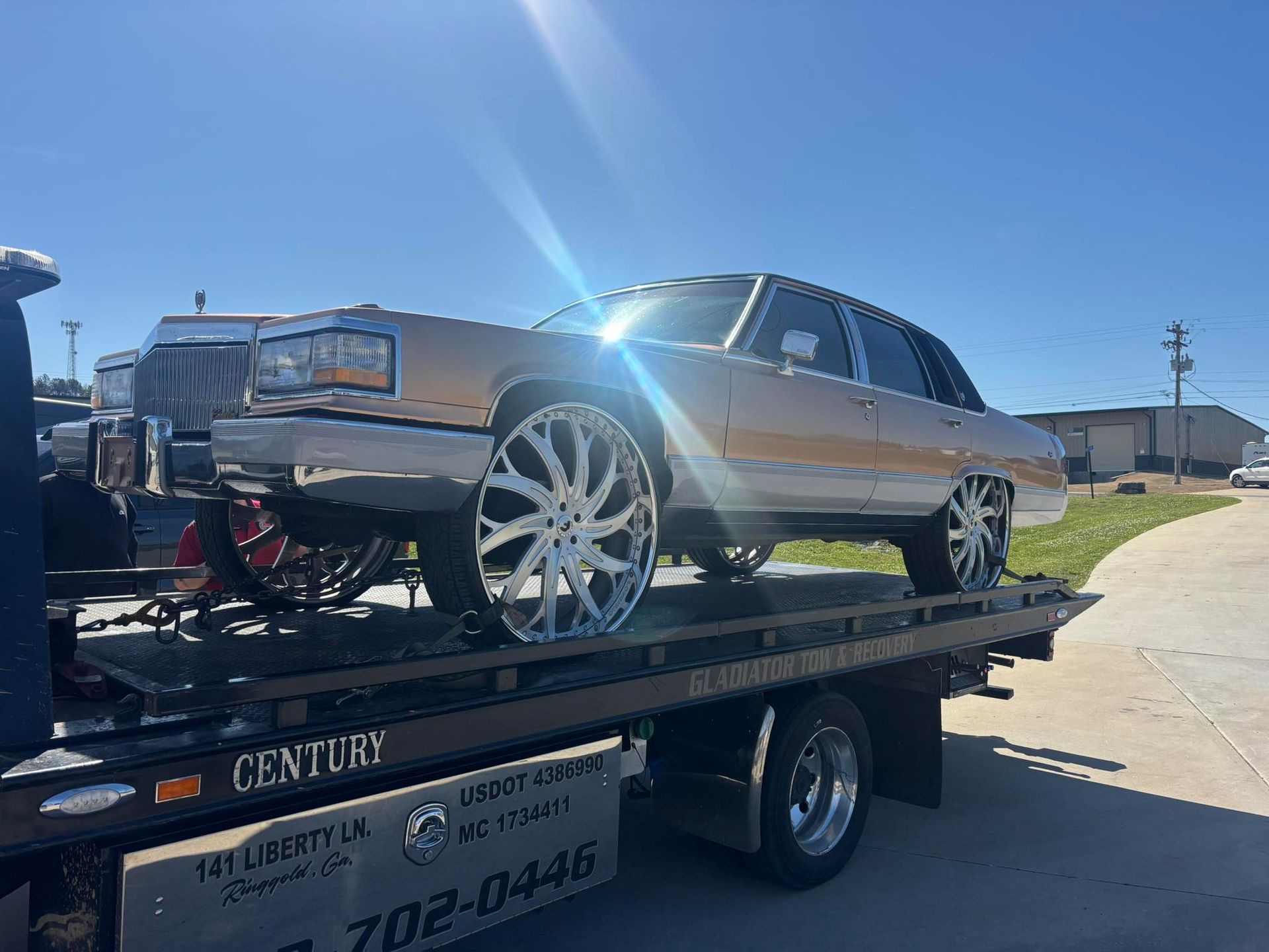 Lowrider car on a trailer under bright sun, parked in a residential street