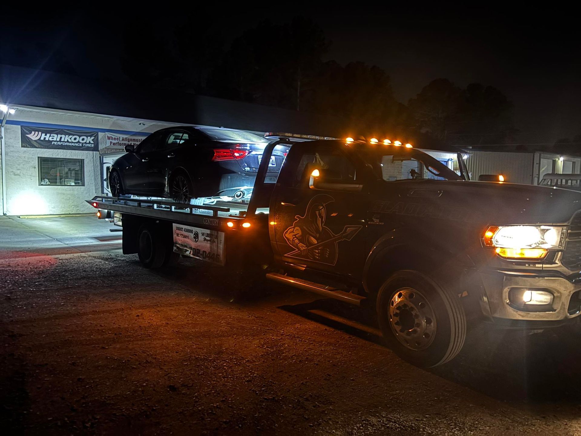Tow truck carrying a black SUV at night outside a lit building