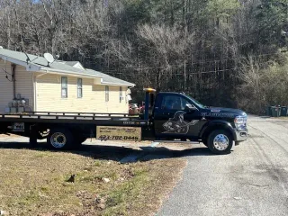 Tow truck hauling a yellow house on a flatbed in a wooded roadside area