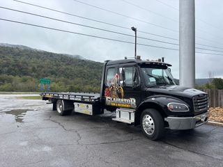 Black tow truck parked on a wet roadside near hills and power lines