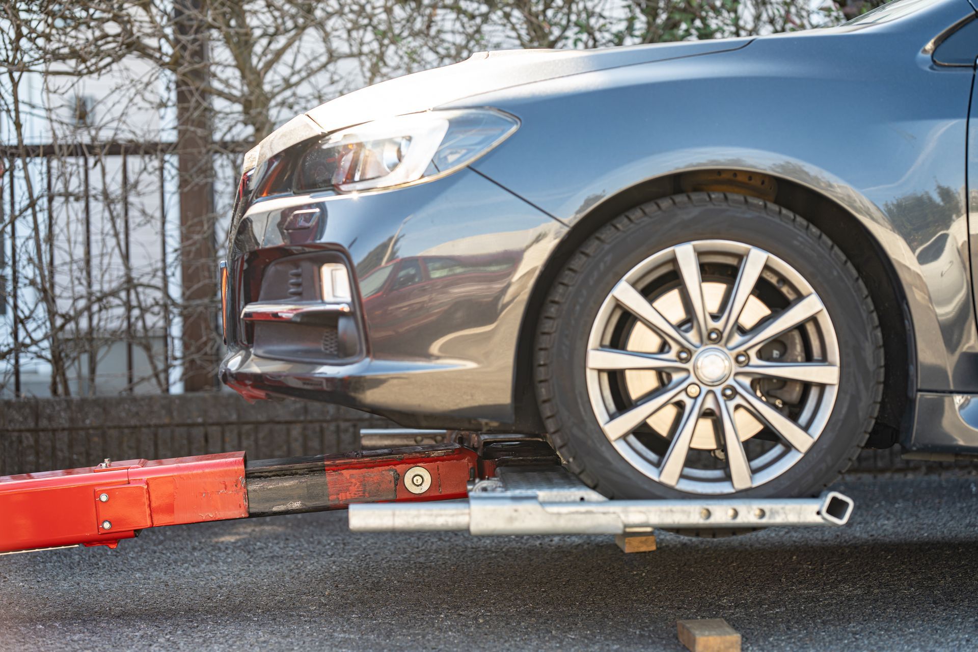 Gray car wheel resting on a tow dolly with red and silver equipment on a road side.