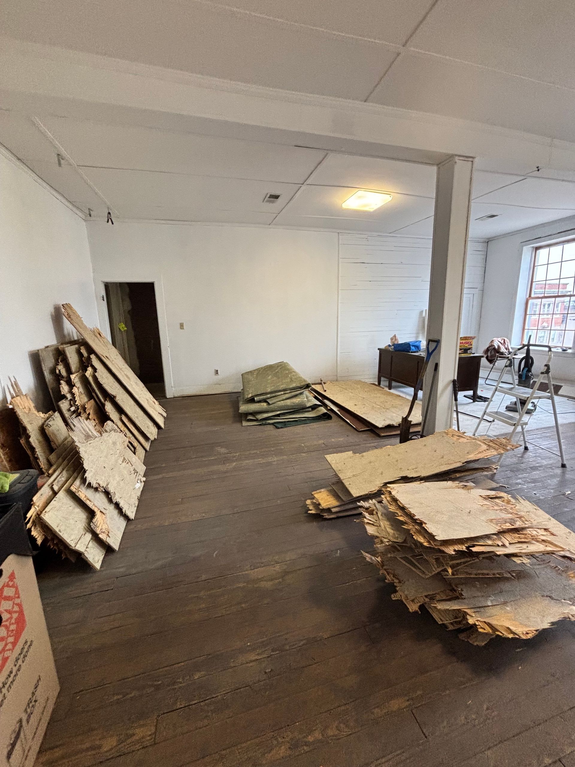 Renovation room with stacked construction debris and wood panels on a dark floor, white walls, and a windowed doorway.