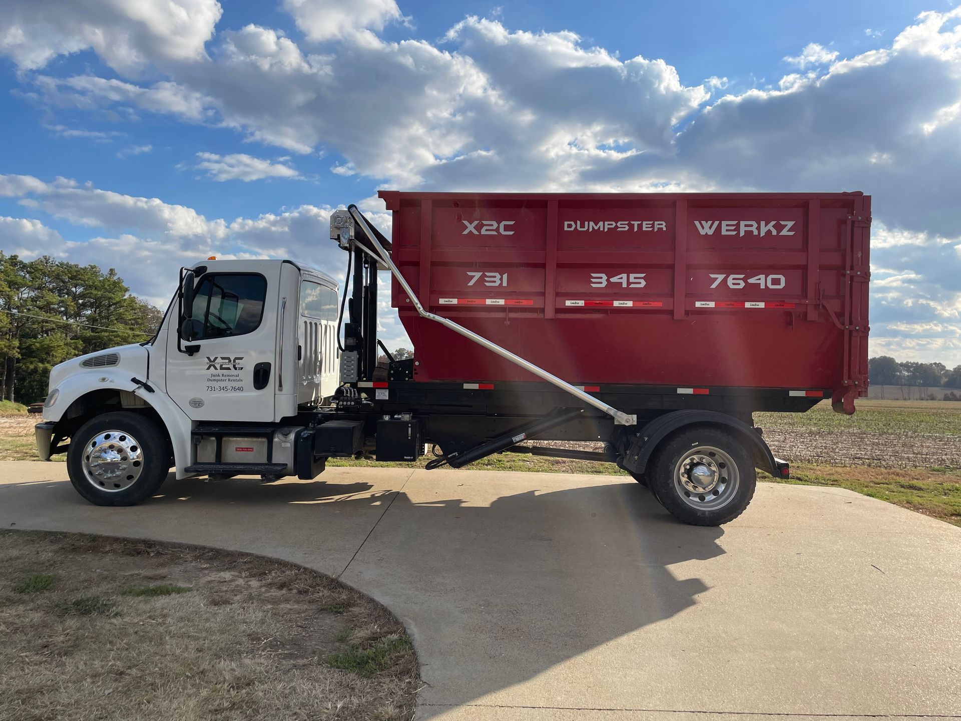 White dump truck with red cargo bed parked outdoors under a cloudy blue sky.