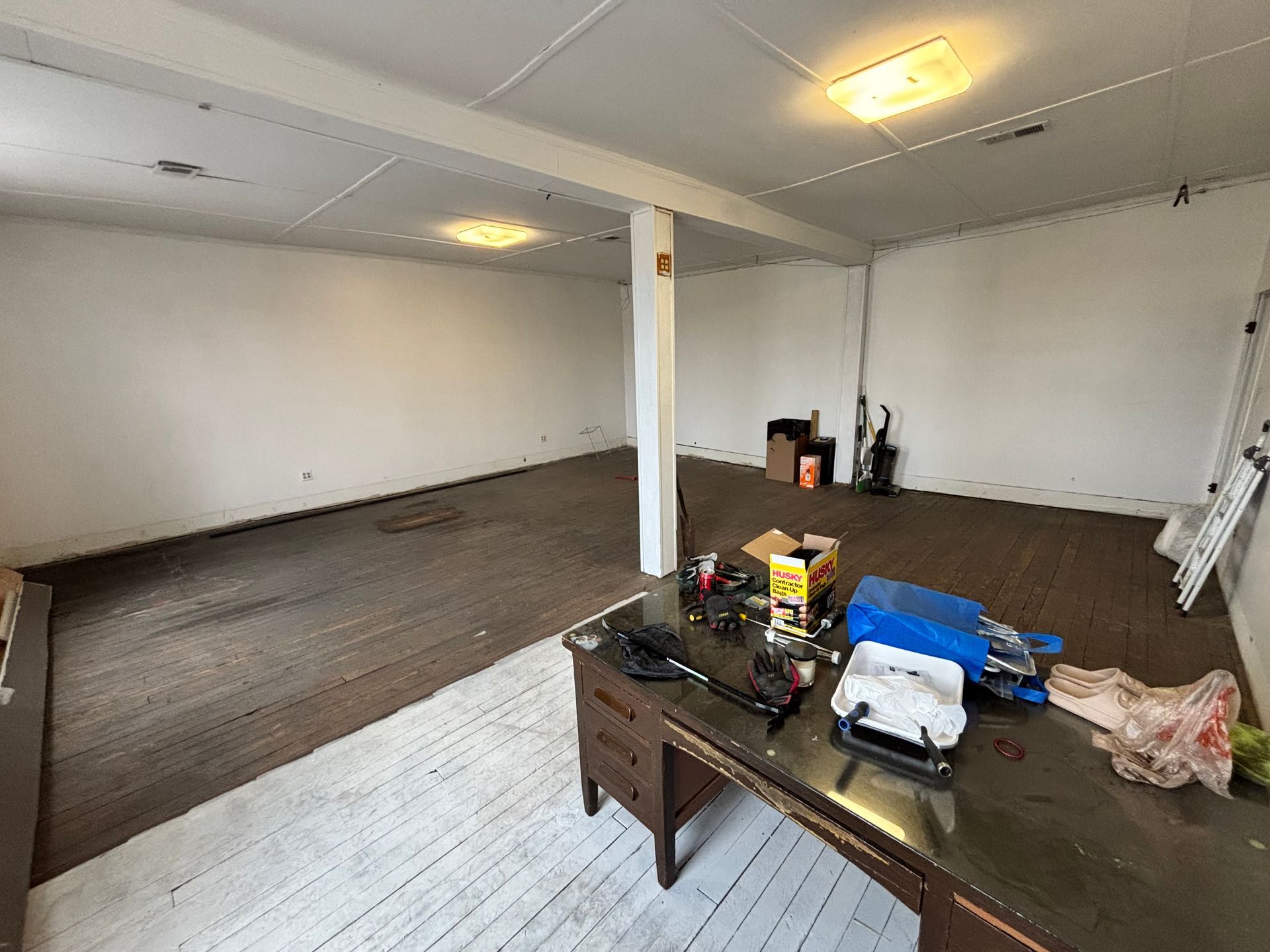 Empty room with two floor surfaces, a table in front, and a ladder leaning against the right wall.