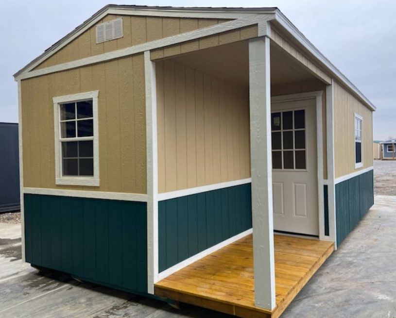 Tan and green shed with porch, white door and trim, window, wooden deck.