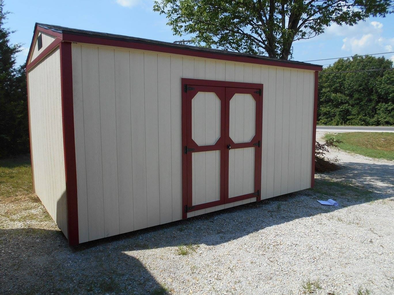 Tan shed with red trim and double doors on gravel.