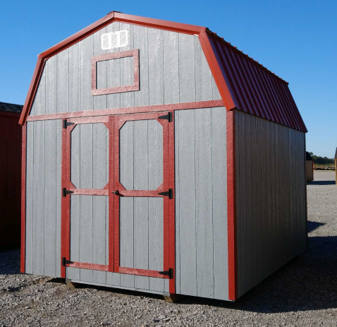 Gray barn-style shed with red trim and roof. Double doors and small window on front. Sunny outdoor setting.