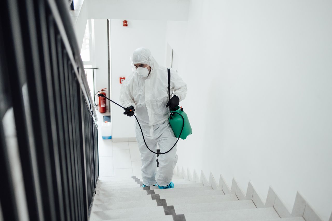 A man in a protective suit is spraying a staircase with a sprayer.