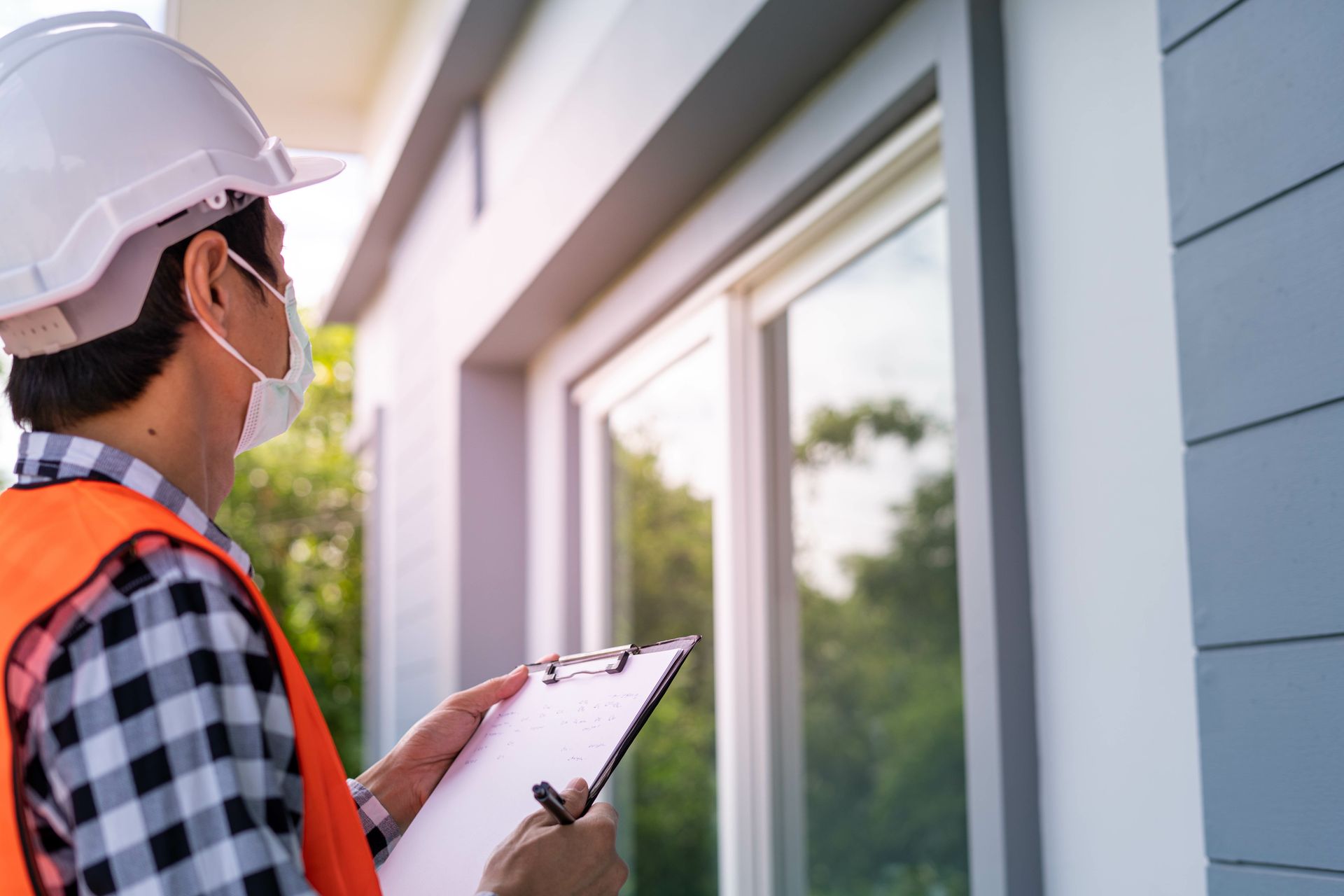 Inspector in hard hat and safety vest taking notes beside a house window