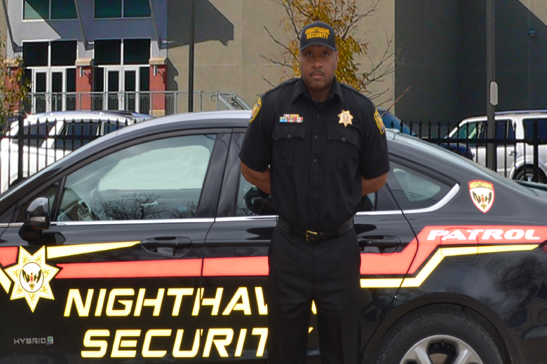 Security guard standing in front of a black patrol car with 