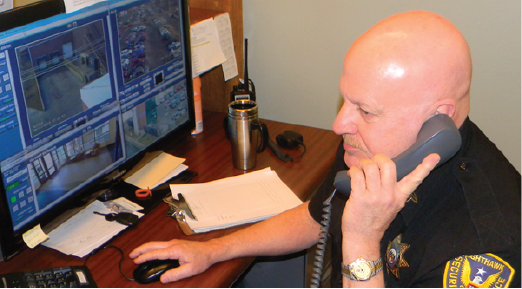 Man on a phone at a desk with multiple computer monitors displaying data and maps