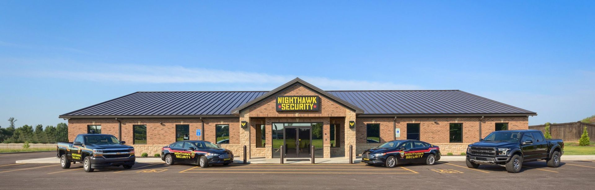 Building with logo and vehicles parked out front on a sunny day.