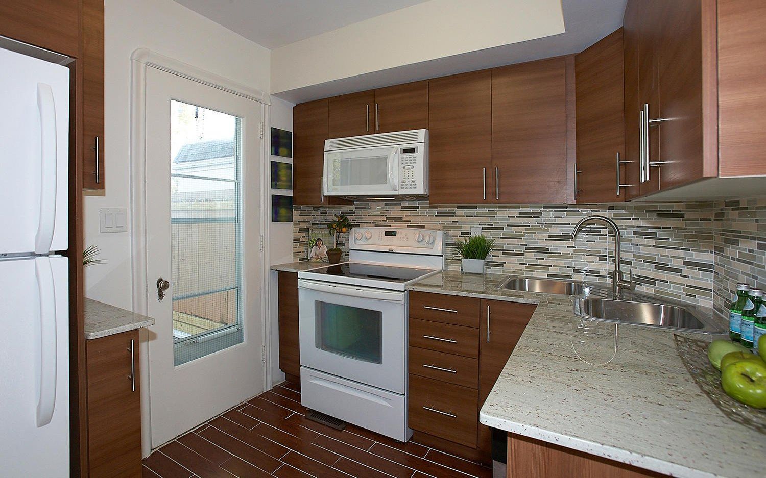A kitchen with wood cabinets, white appliances, speckled granite countertops, a mosaic backsplash, and a glass door.