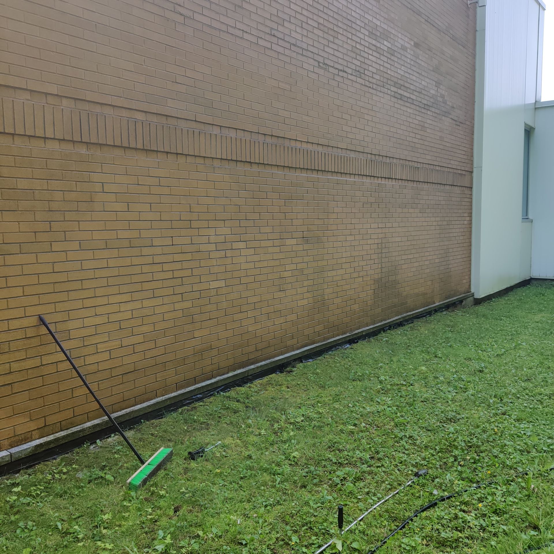 Un balai vert est posé sur l'herbe devant un mur de briques