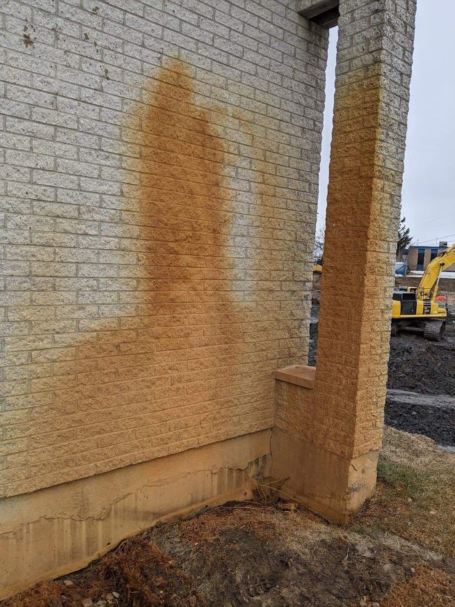 Un mur de briques avec des taches brunes dessus et une excavatrice jaune en arrière-plan.