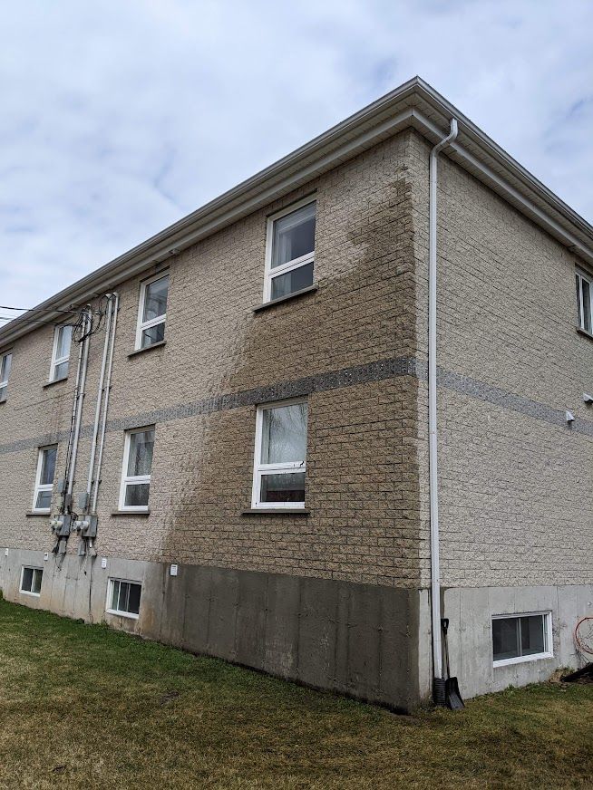 Un grand bâtiment en briques avec beaucoup de fenêtres se trouve au sommet d'un champ vert luxuriant.