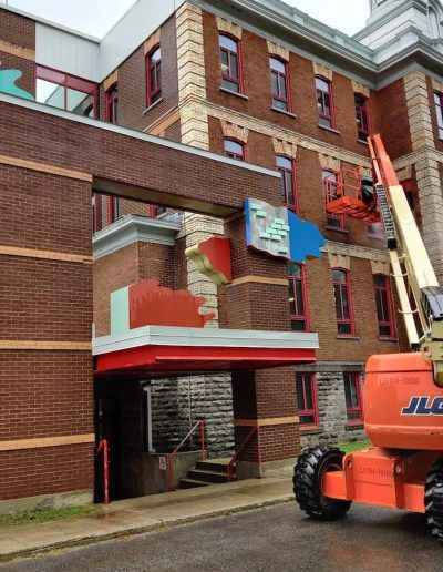 Un ascenseur JLG orange est garé devant un grand bâtiment en briques