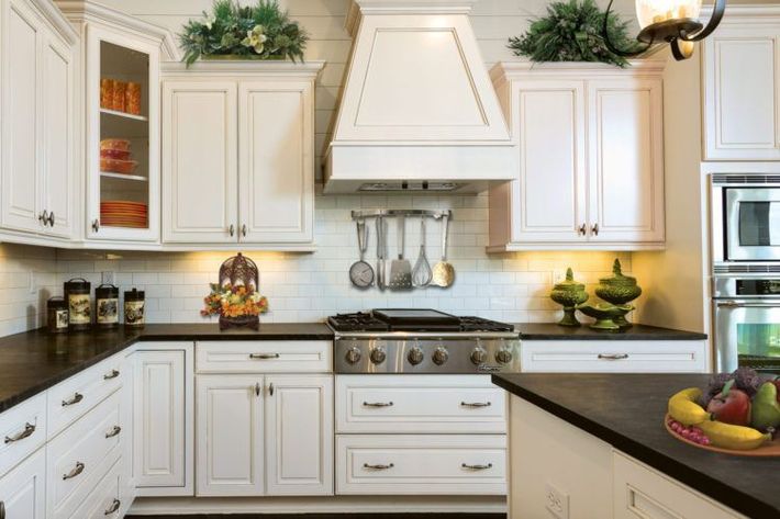 Bright white kitchen with black countertops, stainless range, and potted greenery on top of cabinets