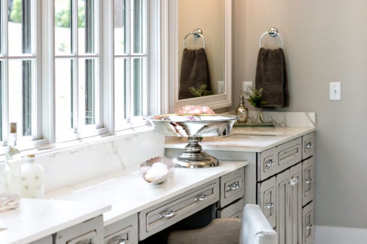Bright bathroom vanity with double sinks, large windows, and gray cabinets.