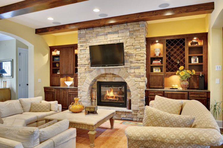 Cozy living room with stone fireplace, built-in shelves, and beige patterned sofas