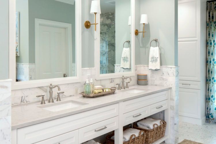 Bright white bathroom vanity with dual mirrors, sink, sconces, and woven baskets underneath