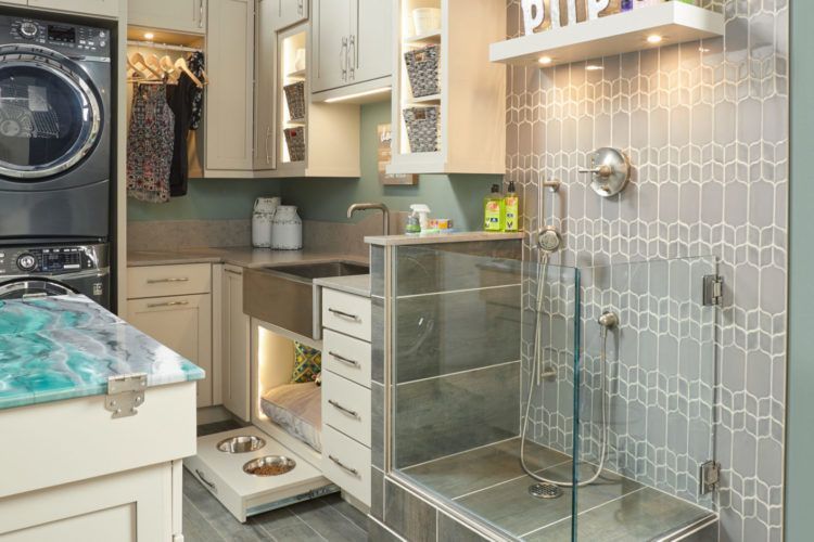 Laundry room with stacked washer and dryer, beige cabinets, and glass shelving beside a tiled shower area